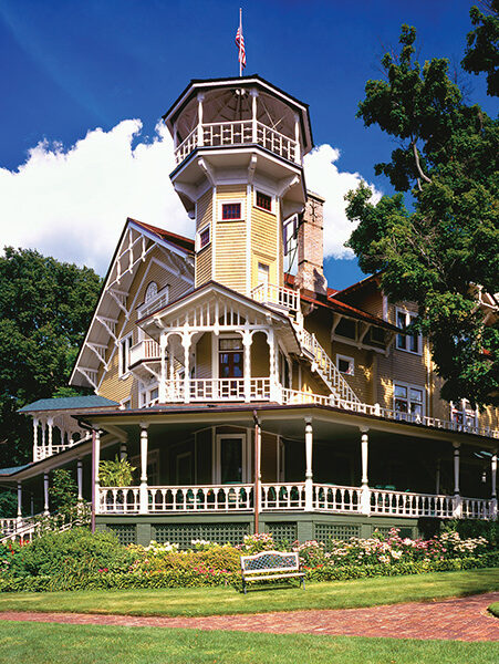 A bright sunny shot of the Black Pointe Estate with its yellow siding, white railing balconies, and turret!